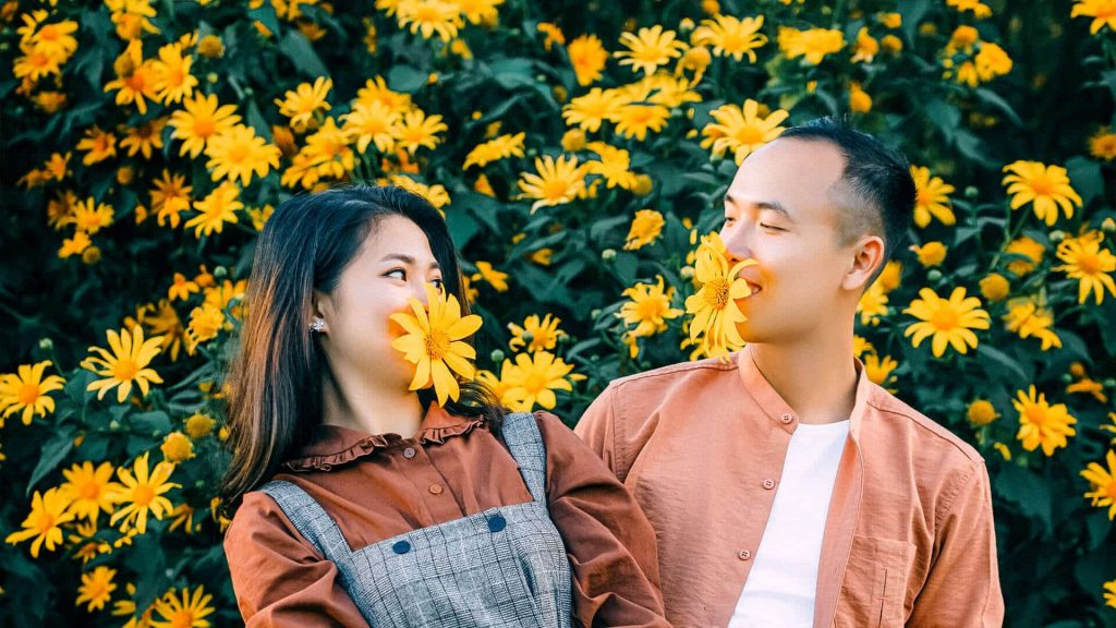 Couple holding daisies in their mouths, having fun - Feel Like a Child in Your Relationship