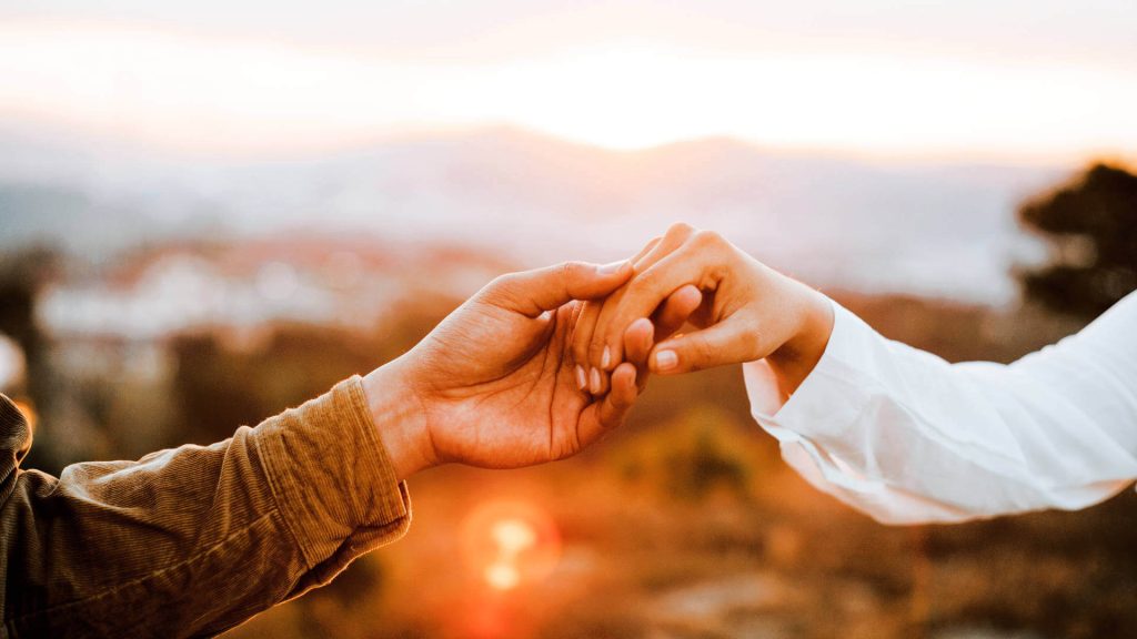 Two hands holding each other at sunset - Attract a High Value Partner