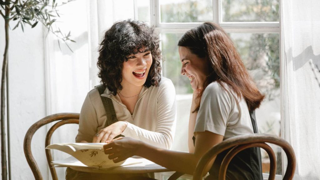 Two women sitting at a table, talking, smiling, healing with ADHD
