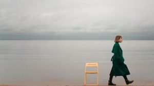 Woman wearing a green coat, walking away from an empty chair, ready to heal
